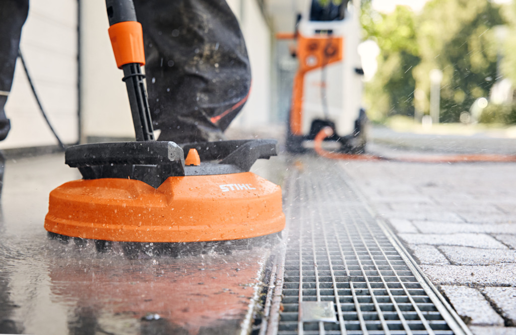 Cleaning tiled area with the STIHL Rotating Wash Brush with a STIHL Water Blaster in the background