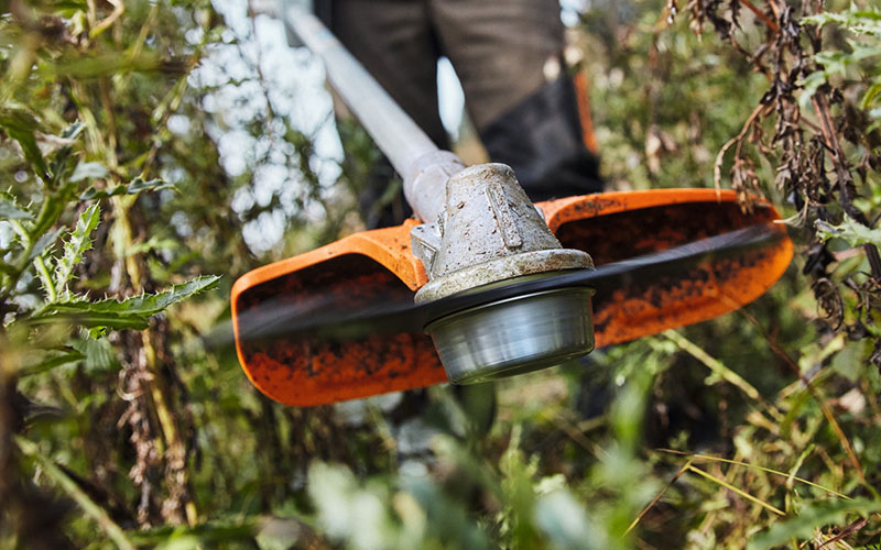 Man on a meadow cutting weed with petrol-driven two-handed handle brushcutter STIHL FS 311 close up cutting blade