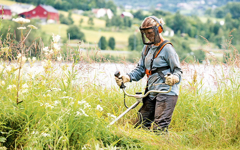 Woman with visor using a petrol burshcutter