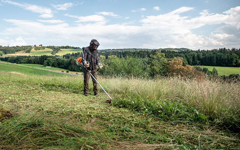 A man using a weedeater to trim a large flat surface